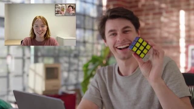 An official Tavus demo still: a split-screen video call where a man holds up a Rubik's cube while the generated persona watches.